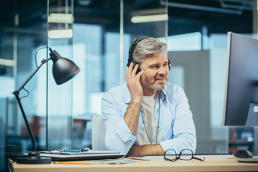 business man at desk listening to earphones smiling