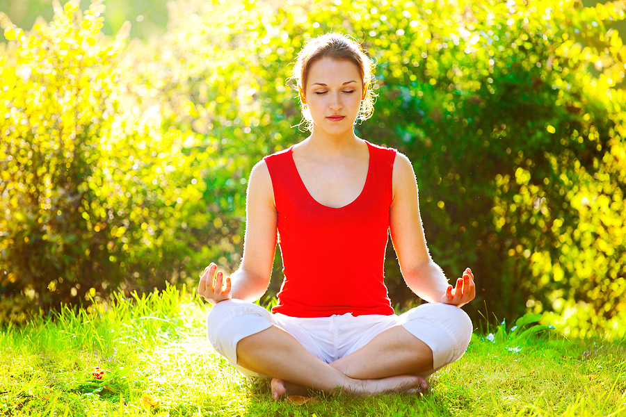 young woman meditating outside in grass