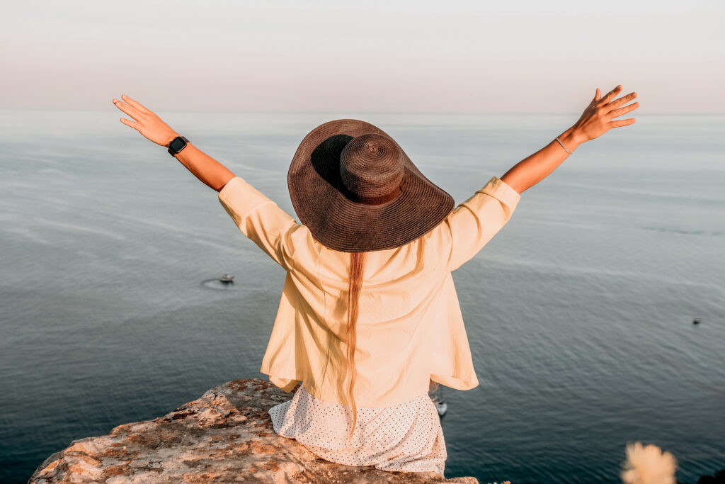 Portrait of happy woman wearing summer black hat with large brim at beach on sunset.