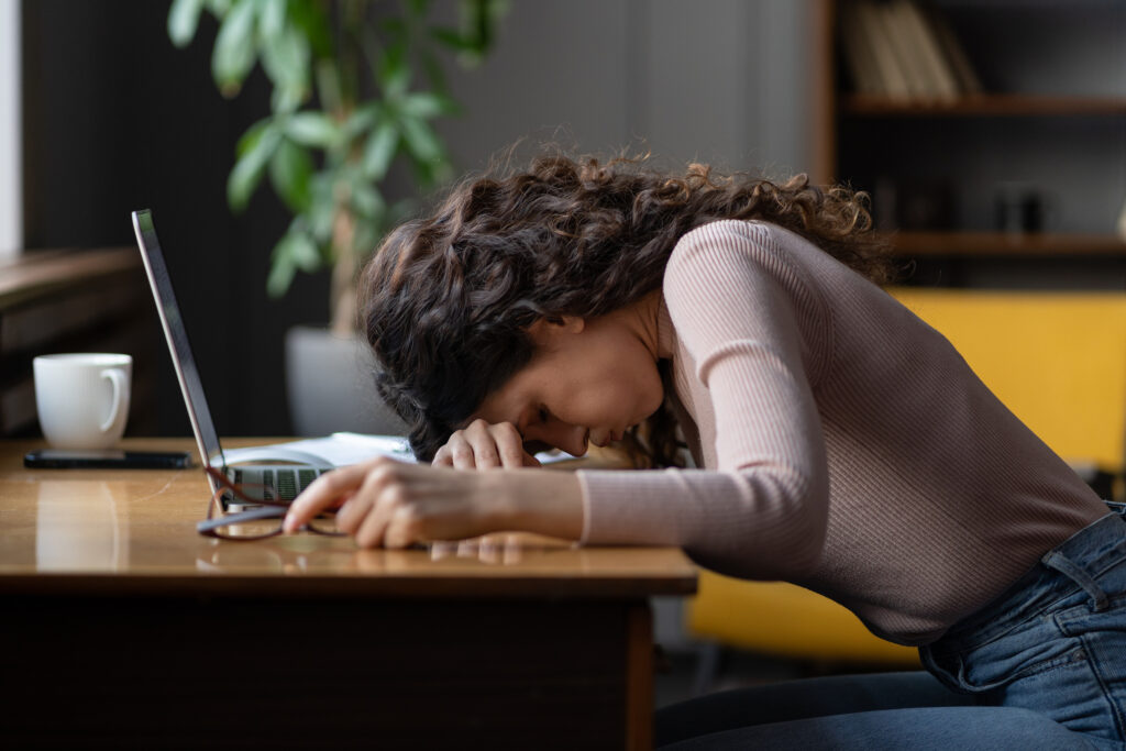 Tired exhausted female resting on her computer because of adrenal fatigue.