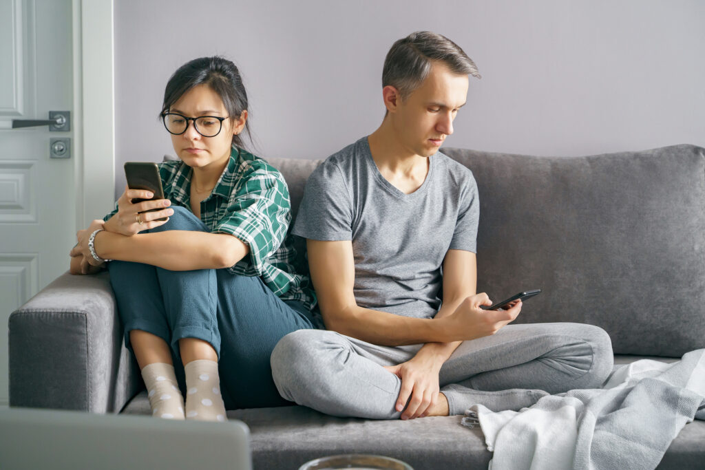 A woman and man sitting on the couch, unmotivated, scrolling on their phones with low drive.