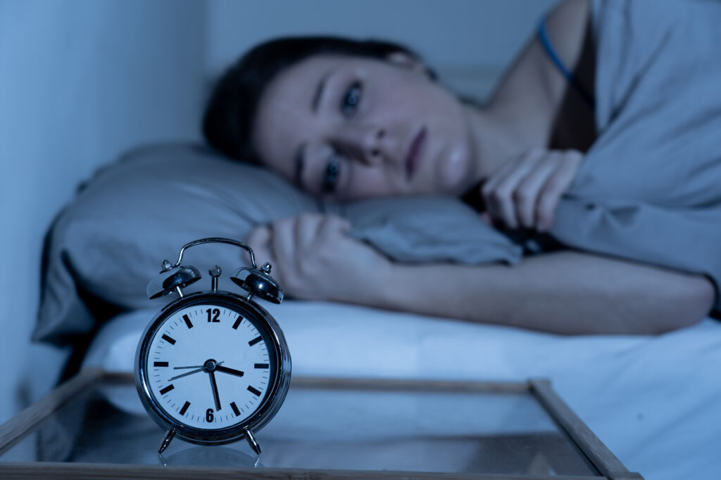 Sleepless and desperate woman awake at night still not able to sleep, feeling frustrated and worried looking at clock suffering from insomnia.